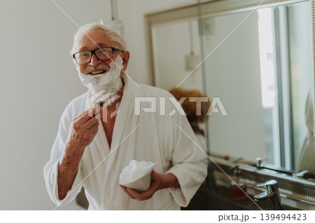 Senior man shaving his beard in the bathroom. Morning routine concept. Senior man shaving his beard in the bathroom. Morning routine concept. 139494423