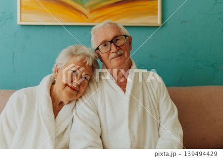 Portrait of happy senior couple sitting together in bathrobe on sofa. Portrait of happy senior couple sitting together in bathrobe on sofa. 139494429