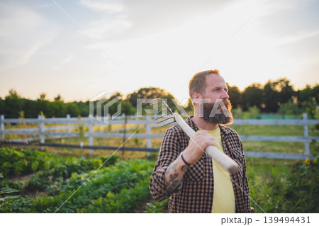 Happy mature farmer man with garden tool outdoors in field. 139494431
