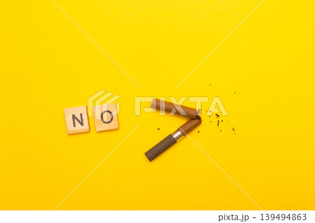 Top view of broken cigarette with the word no on a yellow background closeup Top view of broken cigarette with the word no on a yellow background closeup 139494863