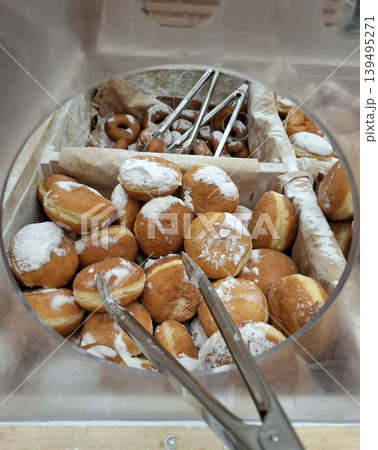 A high angle view shows a wooden bakery bin filled with fresh sugar powdered traditional donuts and pampushky. Metal tongs are placed for serving these sweet treats. A high angle view shows a wooden bakery bin filled with fresh sugar powdered traditional donuts and pampushky. Metal tongs are placed for serving these sweet treats. 139495271