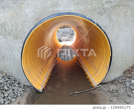A large corrugated plastic drainage pipe is seen from inside, integrated into a concrete wall. This structure is part of infrastructure and sewage system work. Water flows through the pipe opening. A large corrugated plastic drainage pipe is seen from inside, integrated into a concrete wall. This structure is part of infrastructure and sewage system work. Water flows through the pipe opening. 139495275
