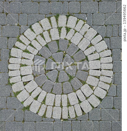 Round paving pattern made with grey stone cobblestones shows green grass growing in the spaces between. This design is suitable for urban landscaping and outdoor pathways. 139495662