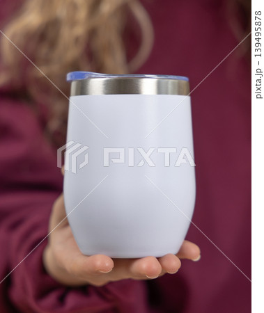 Blank white 12 oz wine tumbler mockup in female hand in dark red sweatshirt, copy space Blank white 12 oz wine tumbler mockup in female hand in dark red sweatshirt, copy space 139495878