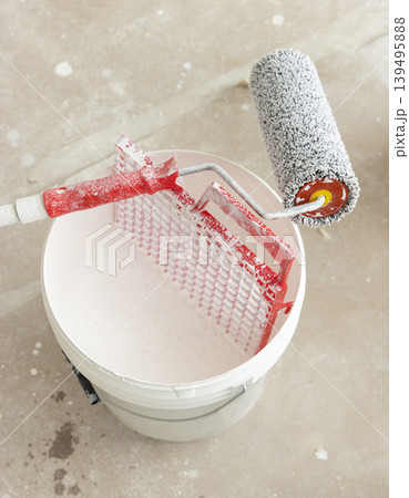 Roller with white paint in bucket during apartment renovation. Construction tools and equipment 139495888