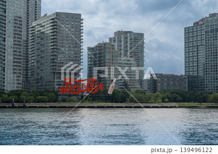 New york, usa august 17,2024. Iconic red pepsi cola sign on long island city waterfront with residential skyline reflected in east river under cloudy summer sky New york, usa august 17,2024. Iconic red pepsi cola sign on long island city waterfront with residential skyline reflected in east river under cloudy summer sky 139496122