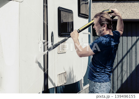 Adult man performing exterior camper washing with water jet outdoors. 139496155
