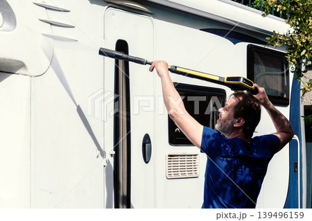 Camper owner washing exterior body of motorhome during seasonal maintenance cleaning. 139496159