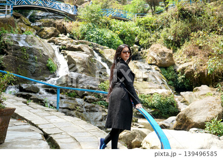 Beautiful woman in black coat posing at Darjeeling Rock Garden waterfall 139496585