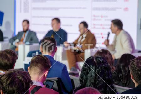 Business panel discussion with engaged audience at conference, professionals listening to speakers on stage Business panel discussion with engaged audience at conference, professionals listening to speakers on stage 139496819