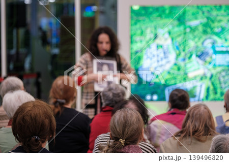 Older adults attend community presentation as woman presenter points to display during educational talk 139496820