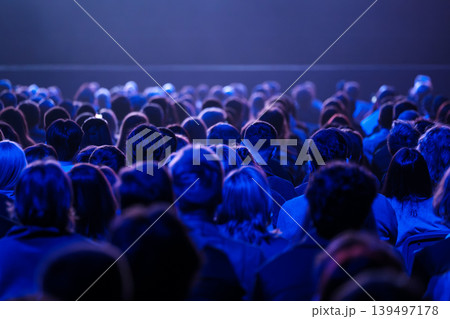 Large audience seated in blue lit auditorium watching live performance and event 139497178