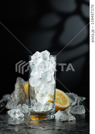 Crushed ice, lemon, and a glass with ice on a black stone table. Crushed ice, lemon, and a glass with ice on a black stone table. 139497370