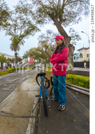 A woman in a red hoodie stands next to a blue bicycle A woman in a red hoodie stands next to a blue bicycle 139498627