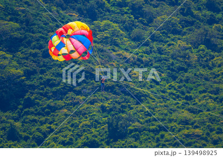 Parasailing at sea in summer on vacation at resort. Extreme water sports. A man parachutes into the sky behind a boat 139498925