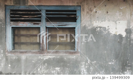 A worn blue window in a cracked concrete wall with peeling paint and a classic texture. A worn blue window in a cracked concrete wall with peeling paint and a classic texture. 139499309