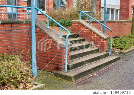 Outdoor stairs made of concrete steps with blue metal handrails, leading up to a building. Outdoor stairs made of concrete steps with blue metal handrails, leading up to a building. 139499739