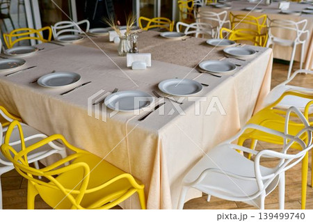 Bright dining setting with modern chairs. Around the table is a row of modern chairs, alternating in bright yellow and crisp white tones for the event. Bright dining setting with modern chairs. Around the table is a row of modern chairs, alternating in bright yellow and crisp white tones for the event. 139499740