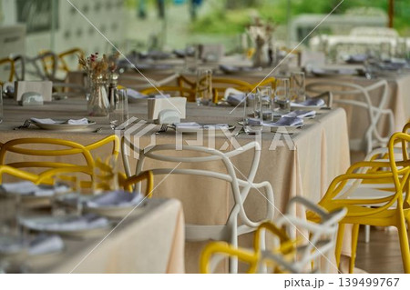 Bright dining setting with modern chairs. Around the table is a row of modern chairs, alternating in bright yellow and crisp white tones for the event. Bright dining setting with modern chairs. Around the table is a row of modern chairs, alternating in bright yellow and crisp white tones for the event. 139499767