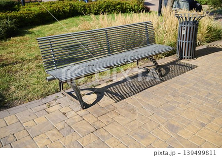 Sunlit park scene showcasing a metal bench casting shadows on stone pavement 139499811