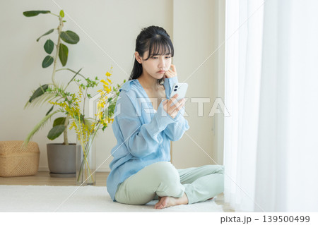スマホを見て悩む女性 139500499