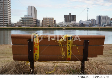 黄色い立入禁止のテープが巻かれた川沿いの木製ベンチ 139500726