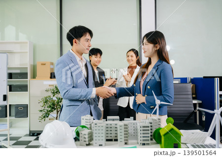 Asian business team collaborating on sustainable city project with wind turbines and housing model. Concept of teamwork, innovation, green energy 139501564