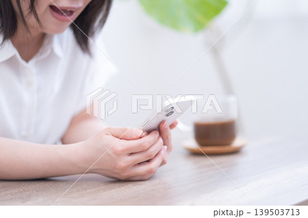 リビングでスマホを操作し驚く女性 リビングでスマホを操作し驚く女性 139503713