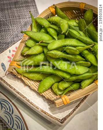 Close up of a woven basket filled with fresh, salted edamame pods Close up of a woven basket filled with fresh, salted edamame pods 139503814