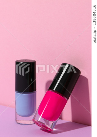 Two nail polish bottles in front of a pink background 139504316