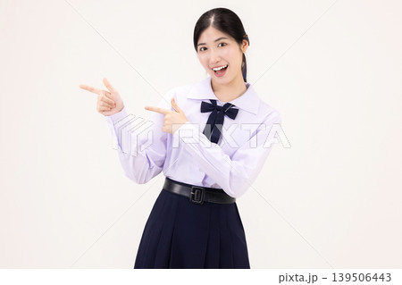 Excited Asian high school student girl in Thai school uniform pointing fingers at copy space for advertising, smiling happily, isolated on white background. Excited Asian high school student girl in Thai school uniform pointing fingers at copy space for advertising, smiling happily, isolated on white background. 139506443