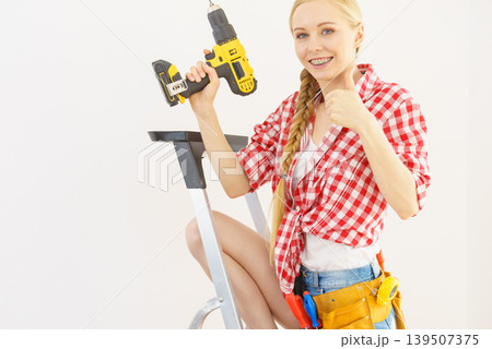 Woman on ladder using drill 139507375