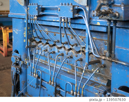 Close-up of a blue industrial metal leveler machine with a complex hydraulic system of pipes and valves. Heavy-duty manufacturing equipment Close-up of a blue industrial metal leveler machine with a complex hydraulic system of pipes and valves. Heavy-duty manufacturing equipment 139507630