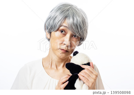 パンダのぬいぐるみを持ち斜め上に視線を投げる白髪のシニア女性 パンダのぬいぐるみを持ち斜め上に視線を投げる白髪のシニア女性 139508098