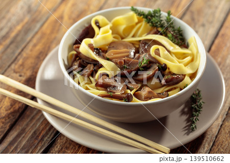 Shimeji and shiitake mushrooms stir-fried with soy sauce, garlic and thyme, served with noodles in a ceramic bowl. Shimeji and shiitake mushrooms stir-fried with soy sauce, garlic and thyme, served with noodles in a ceramic bowl. 139510662