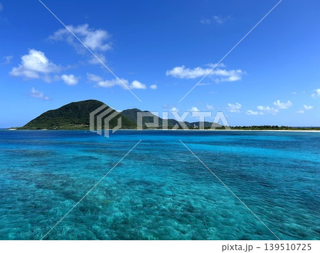 伊平屋島の珊瑚礁が透けるエメラルドの海と緑の山 139510725
