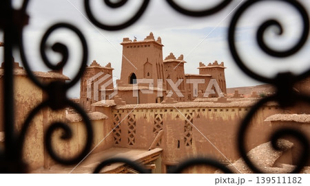 Traditional mud-brick towers and rooftops of a desert kasbah are framed by ornate wrought iron patterns, Traditional mud-brick towers and rooftops of a desert kasbah are framed by ornate wrought iron patterns, 139511182