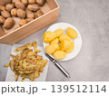 Peeled potatoes on plate, peels, peeler and wooden crate on kitchen counter, copy space 139512114
