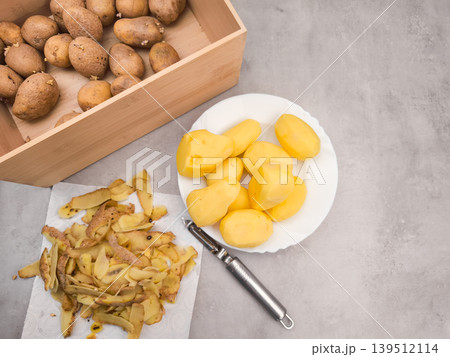 Peeled potatoes on plate, peels, peeler and wooden crate on kitchen counter, copy space Peeled potatoes on plate, peels, peeler and wooden crate on kitchen counter, copy space 139512114