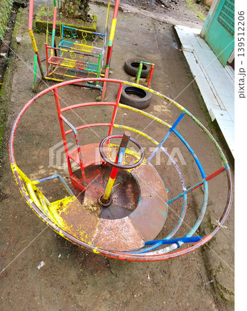 High angle view of a colorful metal merry-go-round and playground equipment on a dirt ground High angle view of a colorful metal merry-go-round and playground equipment on a dirt ground 139512206