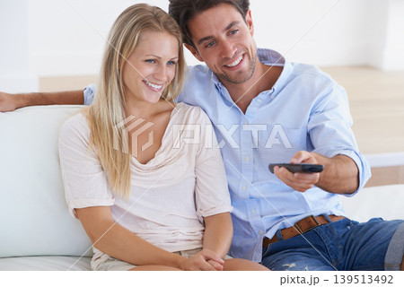 Happy couple, relax and watching TV for entertainment, holiday or weekend together at home. Man and woman smile with remote for streaming movie, series or show in comfort on living room sofa at house 139513492