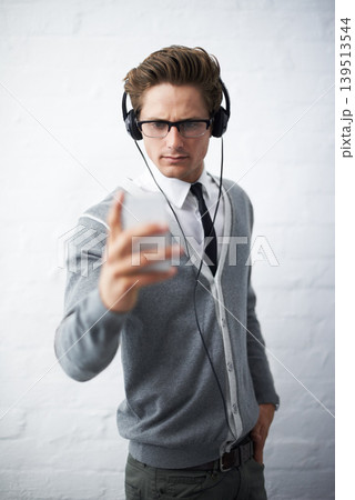 Business man, headphones and phone with texting, reading and listening to music by wall background. Entrepreneur, person or employee with smartphone, audio streaming subscription and social network Business man, headphones and phone with texting, reading and listening to music by wall background. Entrepreneur, person or employee with smartphone, audio streaming subscription and social network 139513544