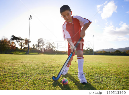 Kid, ball and playing hockey on green grass for game, sports or outdoor practice match. Young child or player enjoying day on field for fitness, activity or training alone in nature with blue sky Kid, ball and playing hockey on green grass for game, sports or outdoor practice match. Young child or player enjoying day on field for fitness, activity or training alone in nature with blue sky 139513560