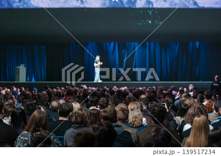 Large conference audience watching keynote speaker on stage during business presentation and public speaking event Large conference audience watching keynote speaker on stage during business presentation and public speaking event 139517234