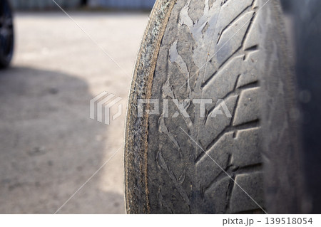 A close view shows a worn out car tire resting on a parking lot surface. The tire surface shows clear signs of wear with little tread remaining A close view shows a worn out car tire resting on a parking lot surface. The tire surface shows clear signs of wear with little tread remaining 139518054
