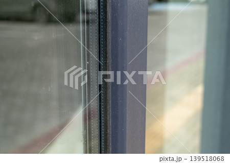 A window frame in a city has visible dirt and a clear reflection of surroundings. It is daytime and people may be passing by 139518068