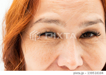 Close-up of a mature woman with red hair and glowing skin. Portrait showing detailed texture around eyes, eyelashes, and natural freckles. Beauty, aging, skincare, and confidence concept. Close-up of a mature woman with red hair and glowing skin. Portrait showing detailed texture around eyes, eyelashes, and natural freckles. Beauty, aging, skincare, and confidence concept. 139518104