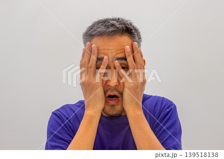 Asian man with hands on head looking shocked and stressed. Expression of negative emotion and mental exhaustion. Concept of burnout, anxiety, workplace pressure and personal crises. Asian man with hands on head looking shocked and stressed. Expression of negative emotion and mental exhaustion. Concept of burnout, anxiety, workplace pressure and personal crises. 139518138