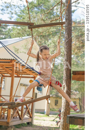 The child overcomes obstacles by walking along a rope track with suspended steps and bridges at a height. Climbing to a height. Safety rope and carabiner The child overcomes obstacles by walking along a rope track with suspended steps and bridges at a height. Climbing to a height. Safety rope and carabiner 139518595