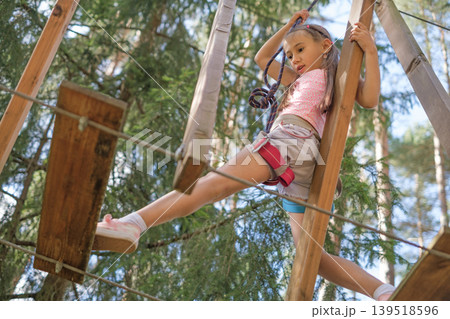 The child overcomes obstacles by stepping on suspended steps located at a distance. Extreme sports. Rope entertainment town in the park 139518596
